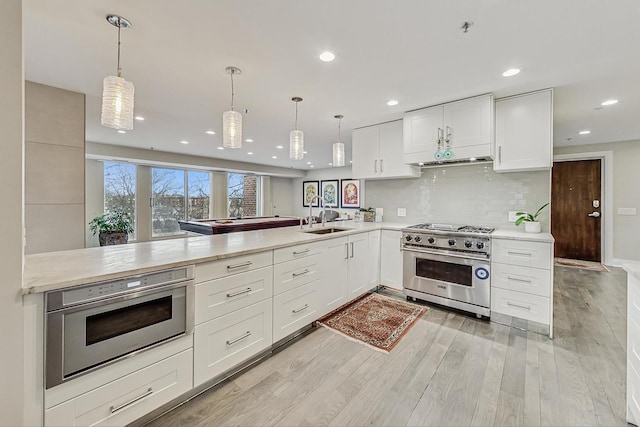 kitchen featuring decorative light fixtures, high end stove, sink, white cabinets, and kitchen peninsula