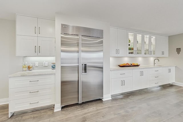 kitchen with sink, light wood-type flooring, white cabinets, and stainless steel built in refrigerator