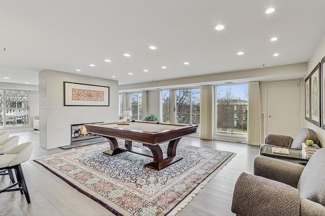 playroom with pool table, a wealth of natural light, light hardwood / wood-style floors, and a multi sided fireplace