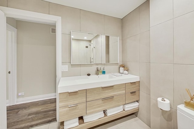 bathroom with tile walls, vanity, toilet, and walk in shower