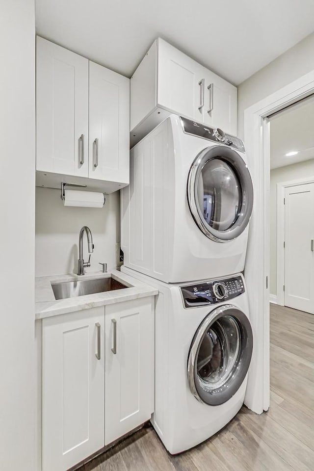 laundry room featuring cabinets, stacked washer and clothes dryer, sink, and light wood-type flooring