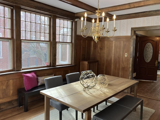 dining space with a notable chandelier, beam ceiling, wood walls, and hardwood / wood-style flooring