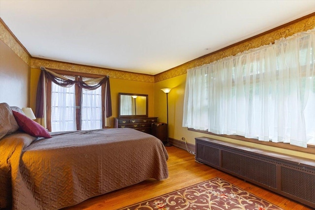 bedroom with multiple windows, radiator, and light wood-type flooring