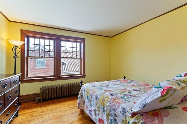 bedroom with crown molding, radiator heating unit, and light hardwood / wood-style floors