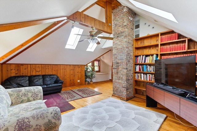 living room featuring ceiling fan, vaulted ceiling with skylight, light hardwood / wood-style floors, and wood walls