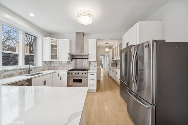 kitchen featuring white cabinets, wall chimney range hood, hanging light fixtures, sink, and appliances with stainless steel finishes