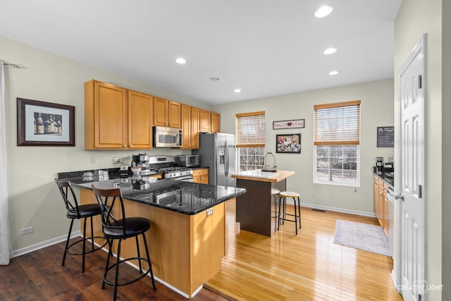 kitchen with light hardwood / wood-style floors, a kitchen island, a kitchen breakfast bar, stainless steel appliances, and dark stone counters