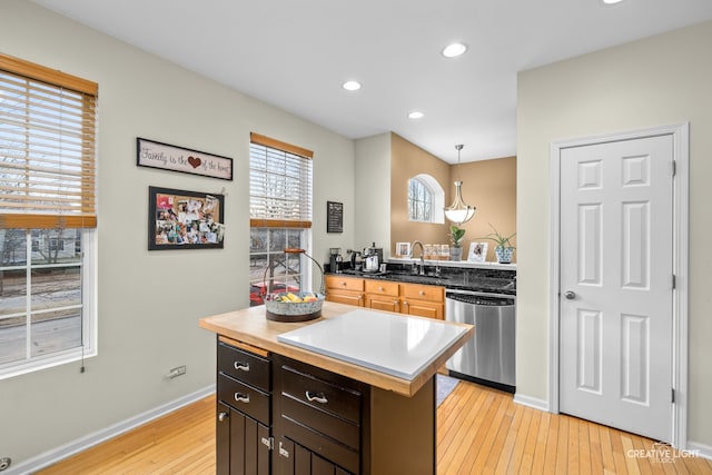 kitchen with light wood-type flooring, pendant lighting, stainless steel dishwasher, dark brown cabinetry, and a center island