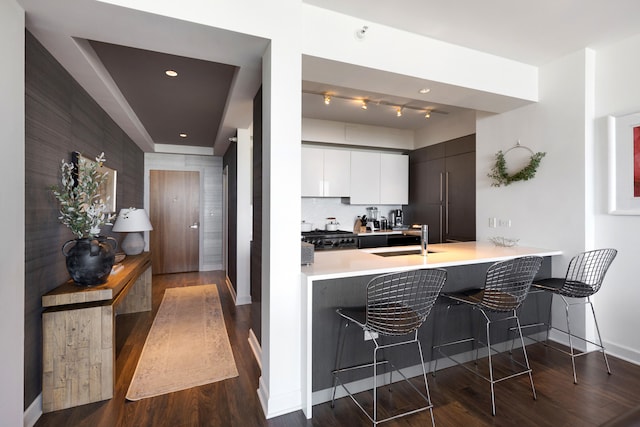 kitchen featuring a kitchen bar, kitchen peninsula, dark hardwood / wood-style flooring, sink, and white cabinets