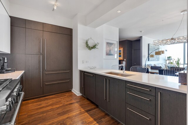 kitchen featuring high end range, kitchen peninsula, dark brown cabinets, sink, and dark hardwood / wood-style floors