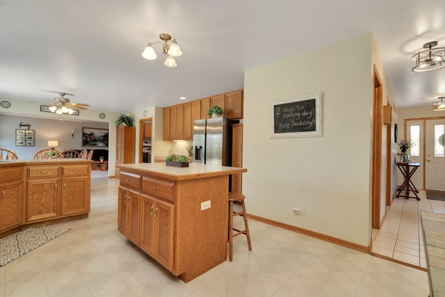 kitchen with a kitchen breakfast bar, ceiling fan with notable chandelier, wall oven, a kitchen island, and stainless steel fridge with ice dispenser