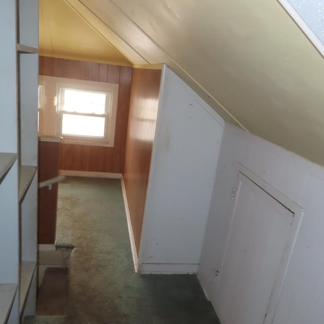 additional living space featuring dark colored carpet, wooden walls, and vaulted ceiling