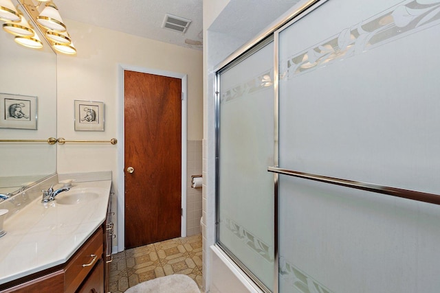 bathroom with vanity, a textured ceiling, shower / bath combination with glass door, and tile walls