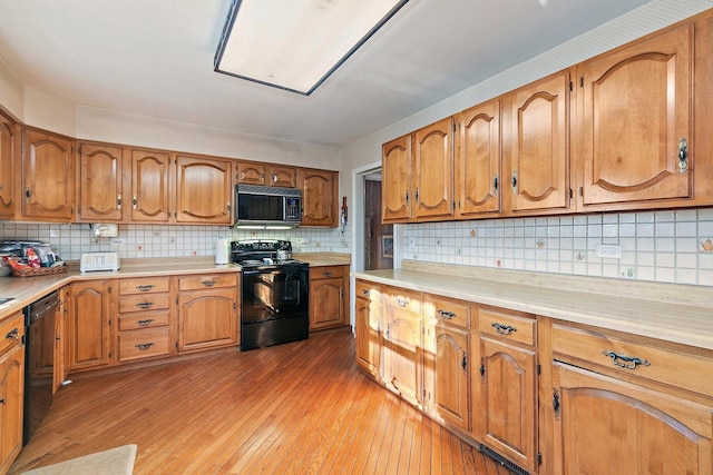 kitchen with light wood-type flooring, decorative backsplash, and black appliances