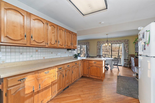 kitchen with light hardwood / wood-style flooring, white refrigerator, a notable chandelier, decorative light fixtures, and kitchen peninsula