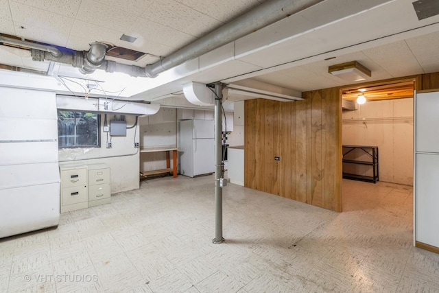 basement with white refrigerator, electric panel, and wooden walls