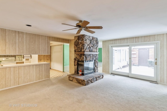 unfurnished living room featuring wooden walls, ceiling fan, a fireplace, and light carpet