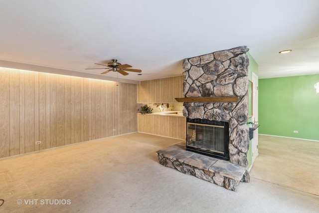 unfurnished living room with ceiling fan, wooden walls, light carpet, and a fireplace