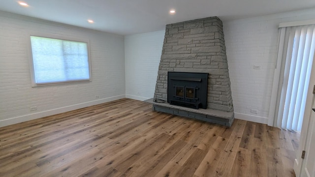 unfurnished living room with hardwood / wood-style floors, a wood stove, crown molding, and brick wall