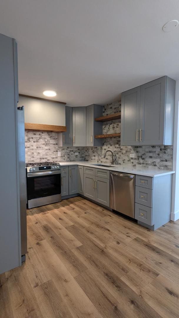 kitchen with gray cabinetry, backsplash, sink, appliances with stainless steel finishes, and light hardwood / wood-style floors