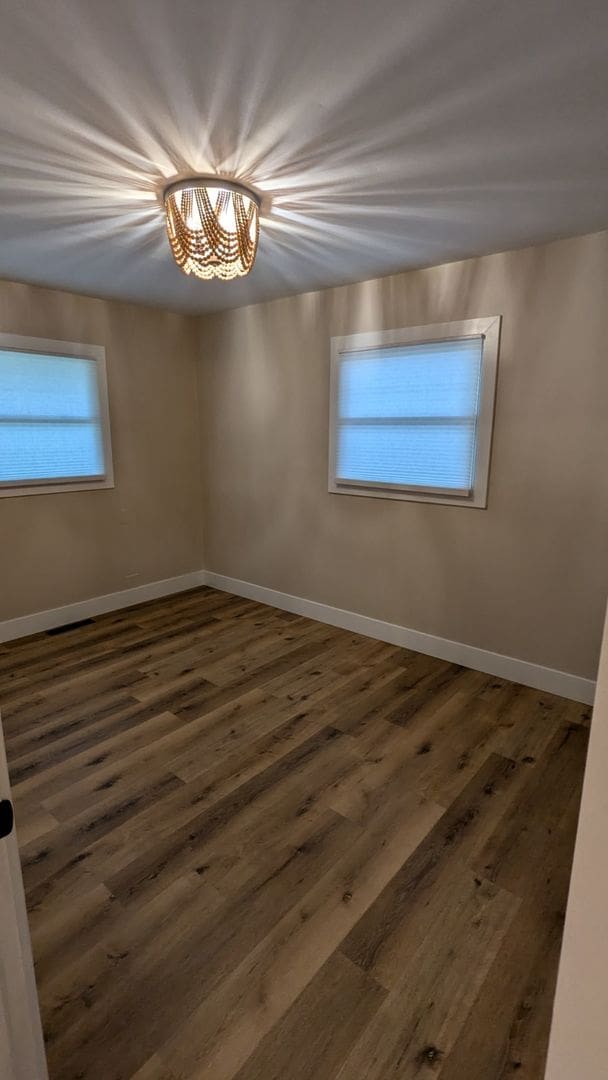 unfurnished room with dark wood-type flooring and an inviting chandelier