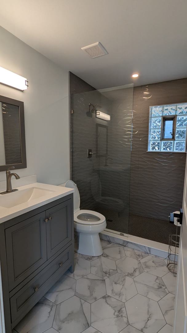 bathroom featuring tiled shower, vanity, and toilet