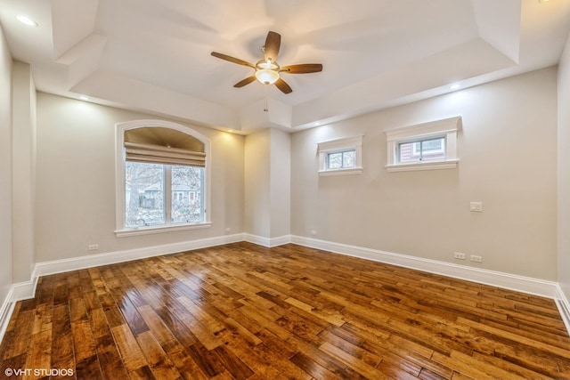 empty room featuring a wealth of natural light, a tray ceiling, ceiling fan, and hardwood / wood-style flooring