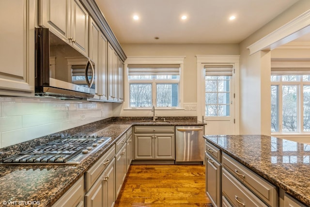 kitchen featuring tasteful backsplash, stainless steel appliances, sink, light hardwood / wood-style flooring, and dark stone countertops