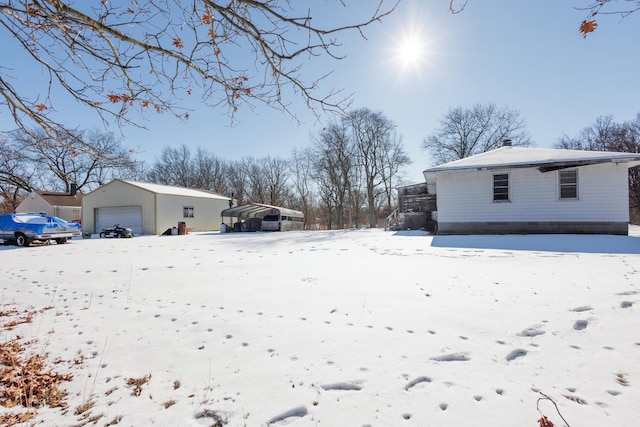 snowy yard featuring a garage, a carport, and an outdoor structure