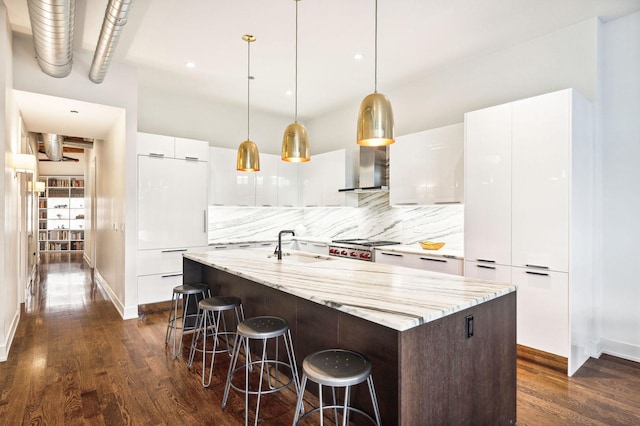 kitchen with light stone countertops, tasteful backsplash, a center island with sink, white cabinetry, and hanging light fixtures