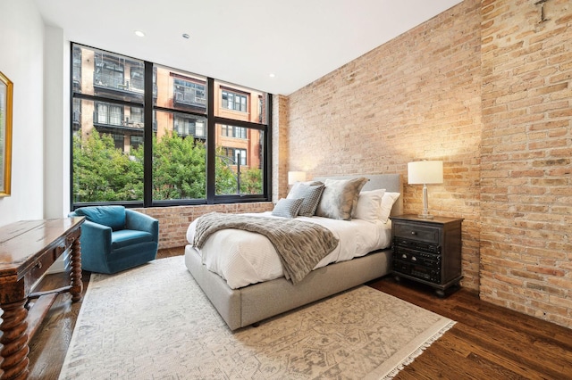 bedroom featuring floor to ceiling windows, wood-type flooring, and brick wall