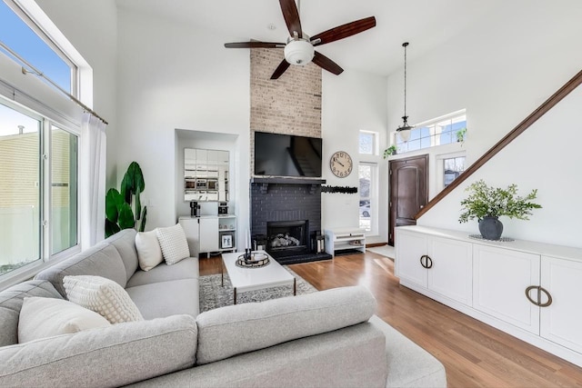 living room with a fireplace, a towering ceiling, light hardwood / wood-style floors, and ceiling fan