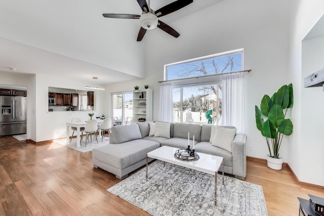 living room featuring a high ceiling, light wood-type flooring, and ceiling fan