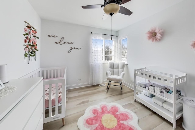 bedroom with ceiling fan, light hardwood / wood-style floors, and a nursery area