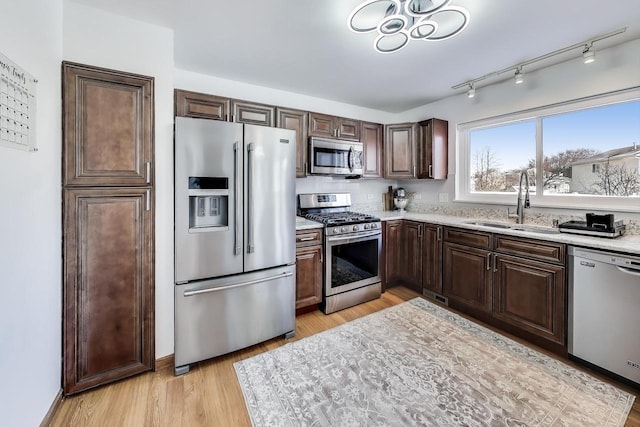 kitchen with light stone countertops, dark brown cabinets, stainless steel appliances, sink, and light hardwood / wood-style floors