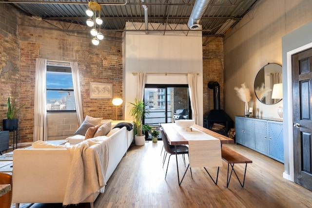 living room featuring a wood stove, brick wall, plenty of natural light, and a towering ceiling