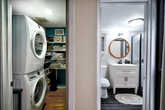 laundry room with sink, dark tile patterned flooring, and stacked washer and dryer