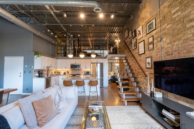 living room with sink, brick wall, a high ceiling, and wood-type flooring