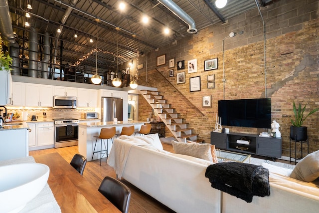 living room with a towering ceiling, brick wall, rail lighting, light wood-type flooring, and sink