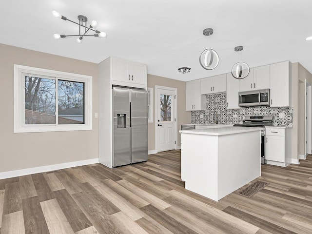 kitchen with appliances with stainless steel finishes, light wood-type flooring, white cabinets, a chandelier, and hanging light fixtures