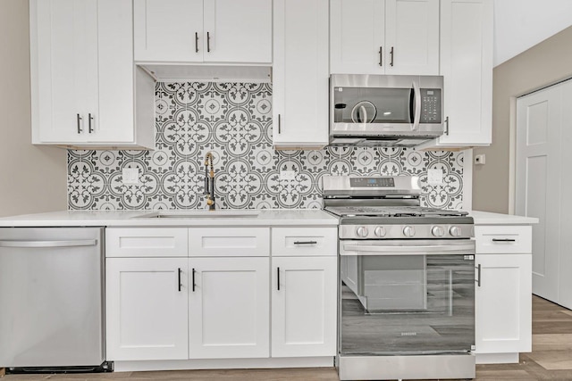 kitchen featuring sink, light hardwood / wood-style flooring, backsplash, white cabinets, and appliances with stainless steel finishes