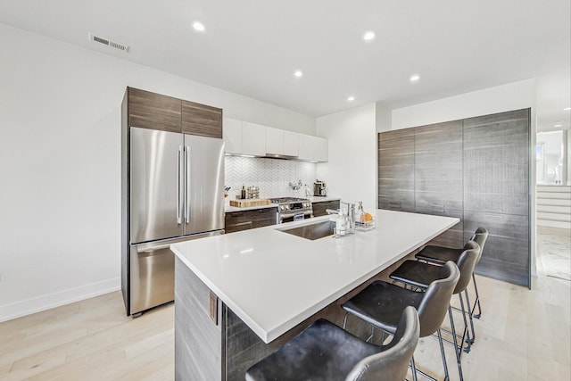 kitchen featuring decorative backsplash, appliances with stainless steel finishes, a breakfast bar, sink, and an island with sink