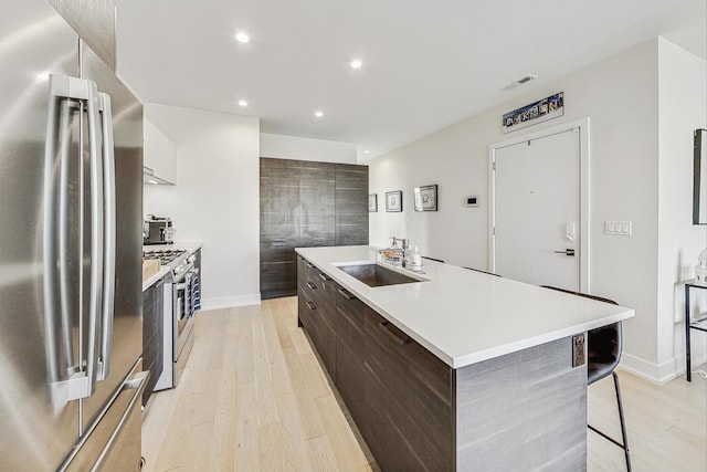 kitchen with sink, stainless steel appliances, an island with sink, a breakfast bar area, and light wood-type flooring