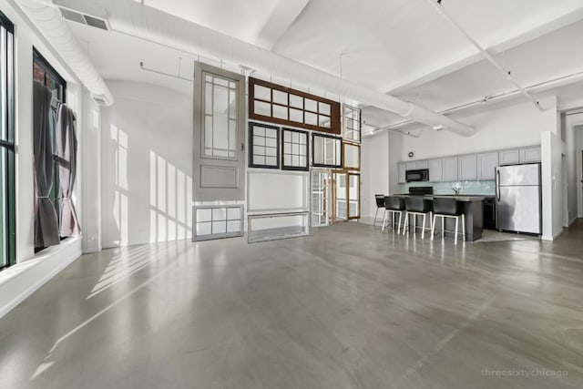 kitchen featuring a high ceiling, stainless steel fridge, concrete floors, a breakfast bar area, and gray cabinets