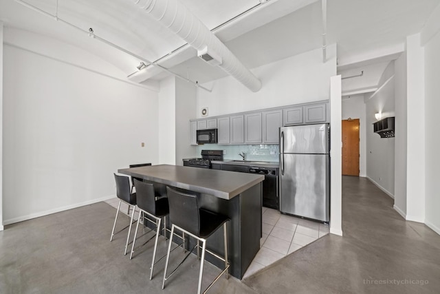 kitchen with a center island, a kitchen breakfast bar, backsplash, gray cabinets, and black appliances