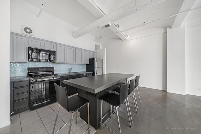 kitchen featuring black appliances, a kitchen breakfast bar, gray cabinets, and backsplash