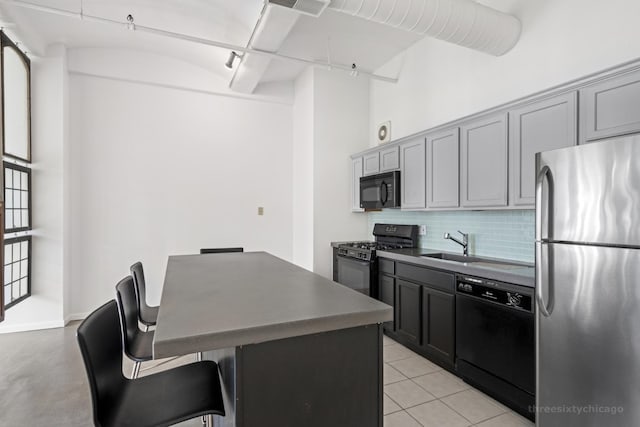 kitchen with a center island, a breakfast bar area, gray cabinets, decorative backsplash, and black appliances