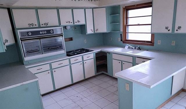 kitchen featuring kitchen peninsula, sink, black appliances, light tile patterned floors, and white cabinets