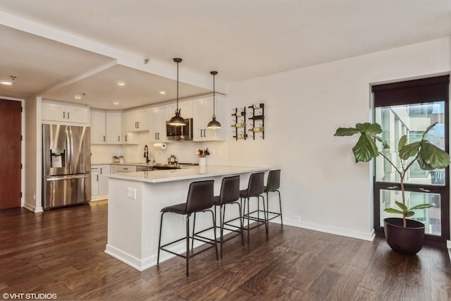 kitchen with kitchen peninsula, pendant lighting, a kitchen bar, white cabinets, and appliances with stainless steel finishes