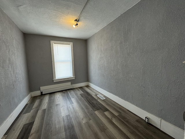 unfurnished room with a textured ceiling, dark hardwood / wood-style floors, and baseboard heating